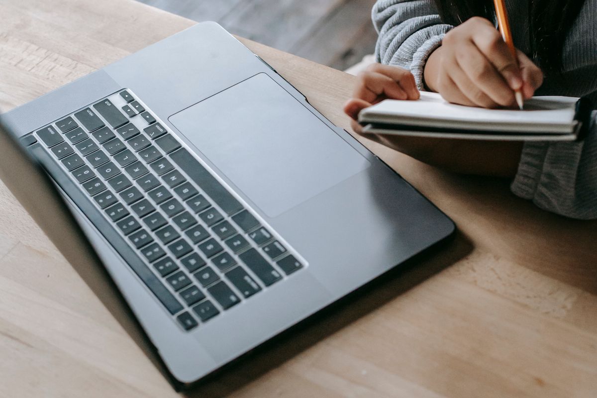 Uczennica w systemie naprzemiennym śledząca zajęcia na wideokonferencji na laptopie i robiąca notatki w zeszycie