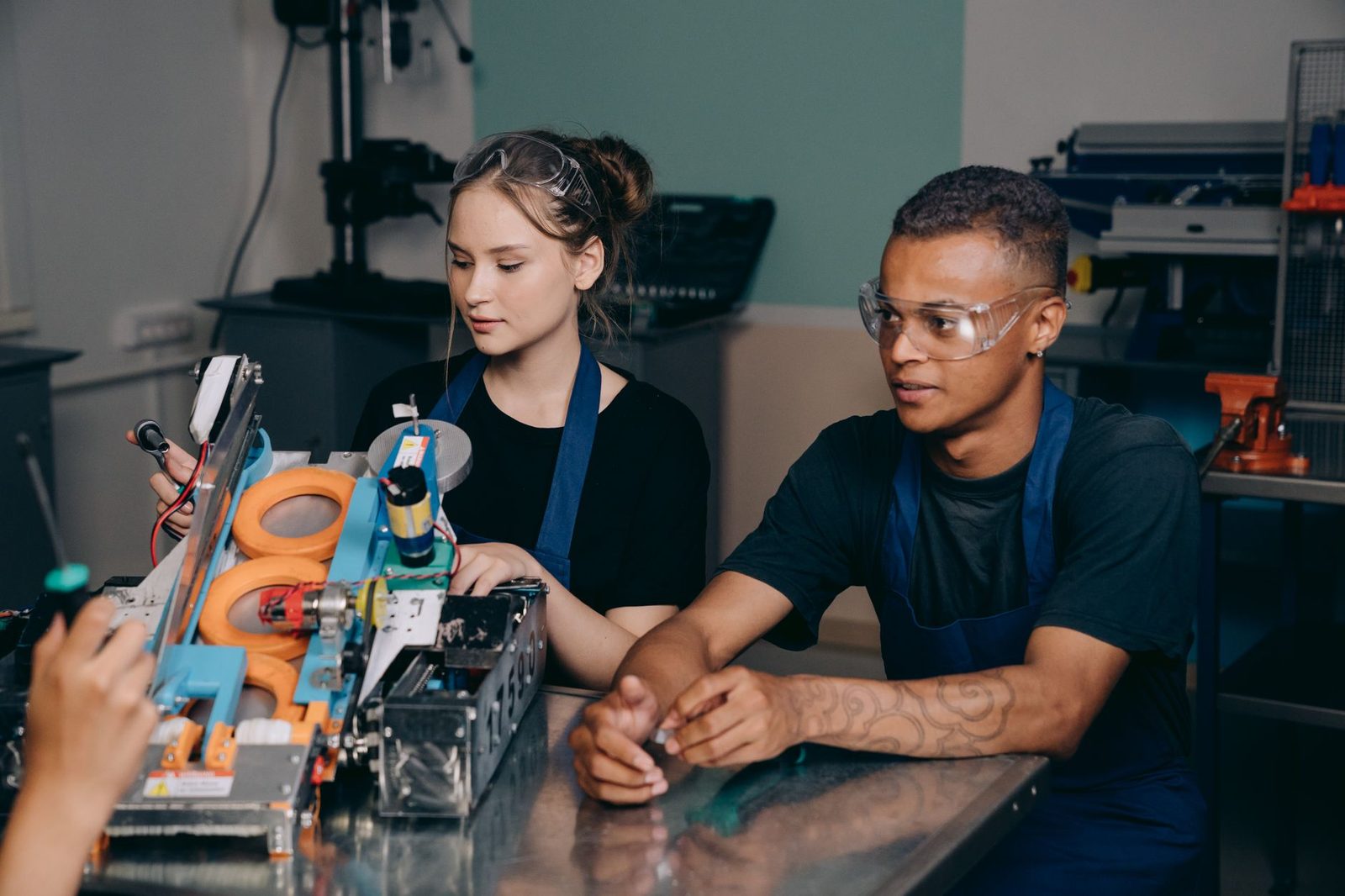 Dois jovens aprendizes de avental e óculos de proteção a trabalhar numa máquina numa oficina