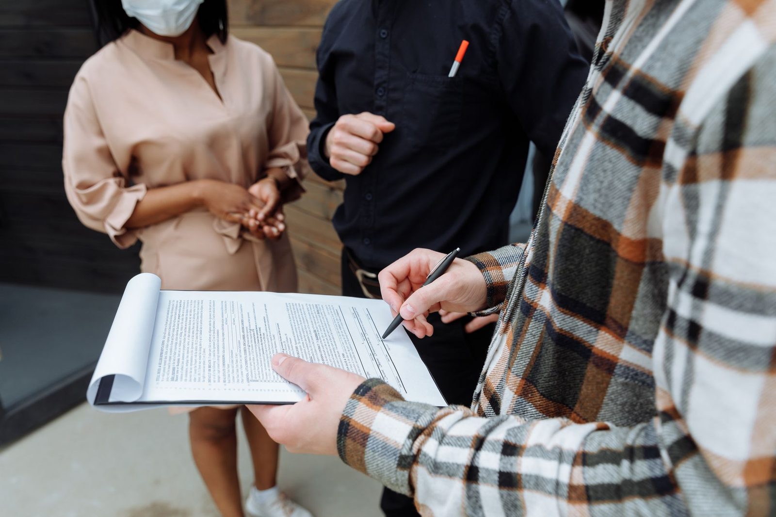 Jong persoon die een contract ondertekent op een klembord tegenover twee andere personen