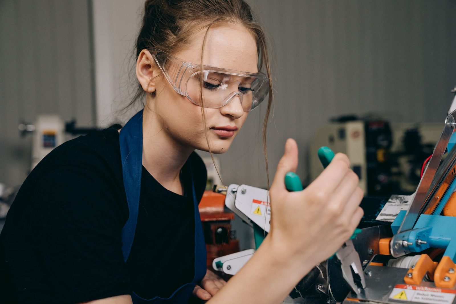Jonge vrouw met veiligheidsbril en schort werkt aan een machine in een werkplaats