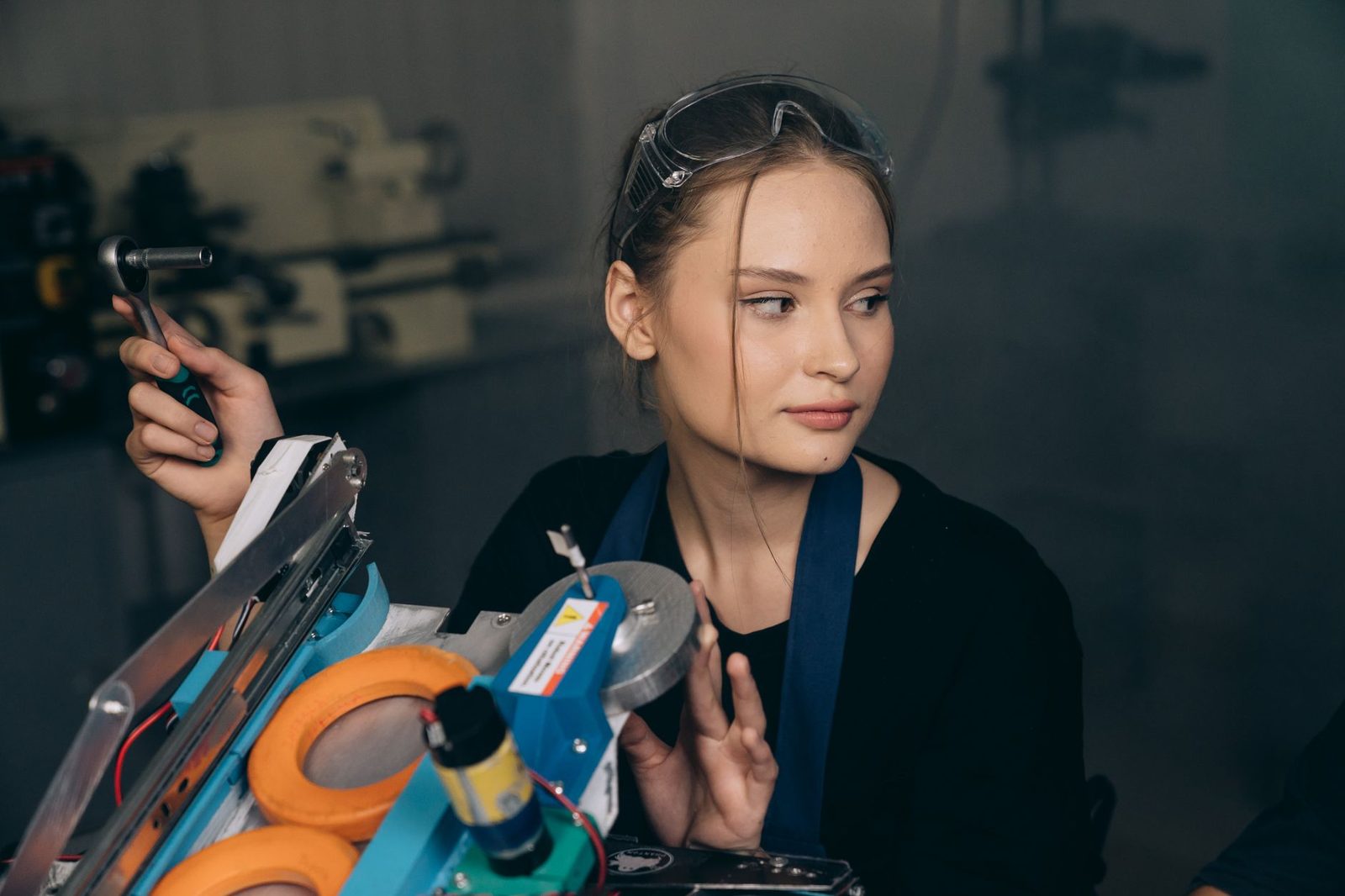 Jeune femme avec lunettes de protection sur la tête tenant une clé à cliquet dans un atelier technique