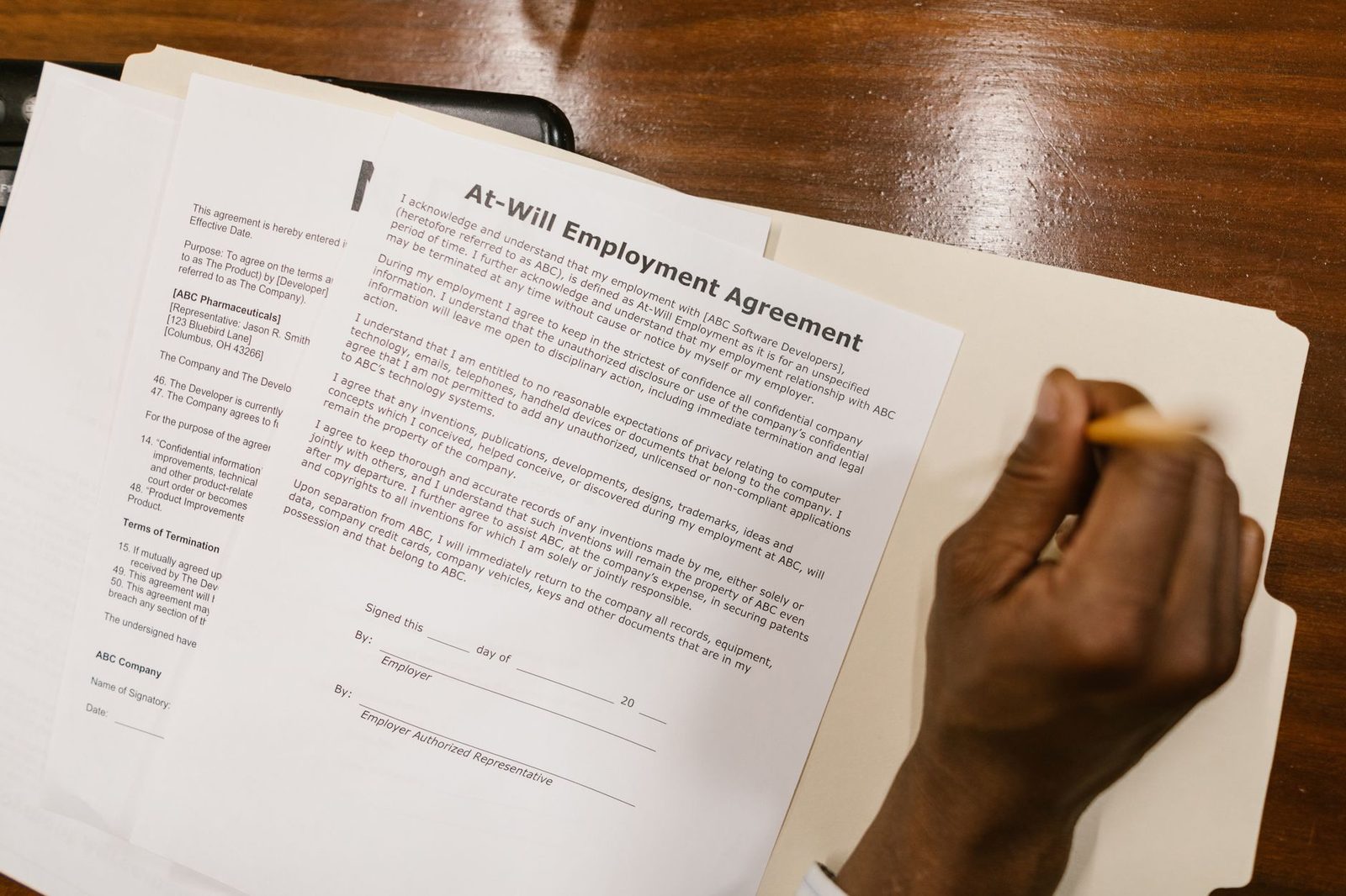 Main tenant un stylo au-dessus d'un contrat de travail posé dans une chemise sur un bureau en bois