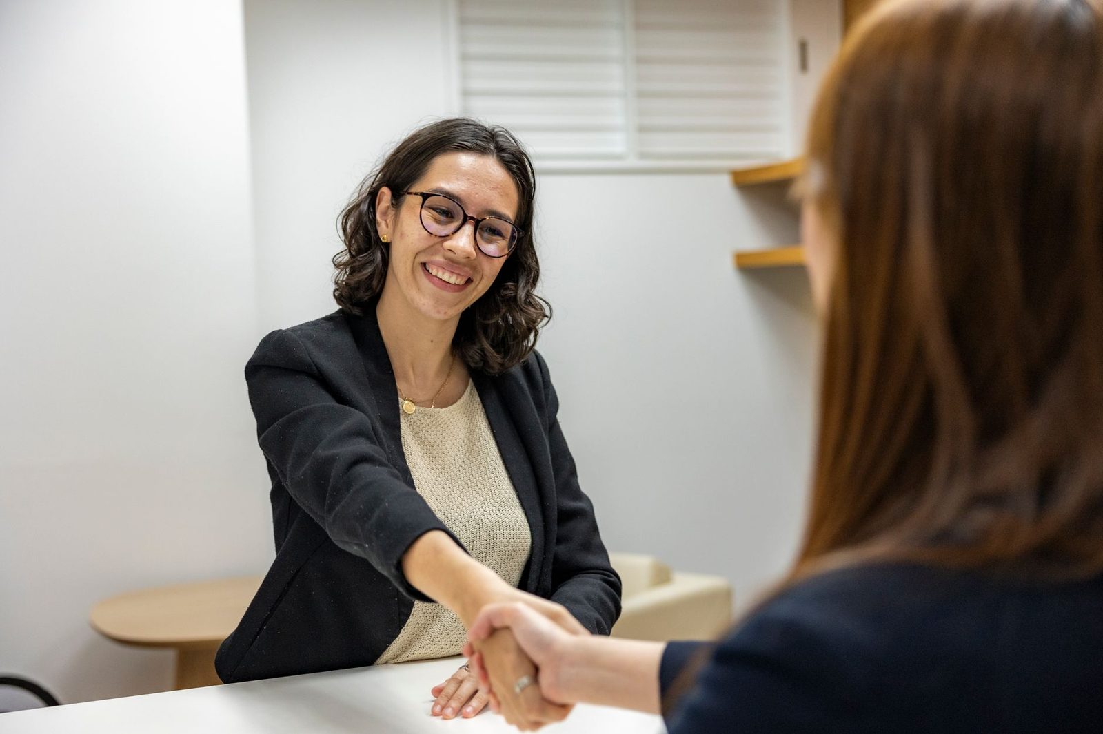 Jeune femme souriante en veste noire serrant la main d'une recruteuse lors d'un entretien d'embauche