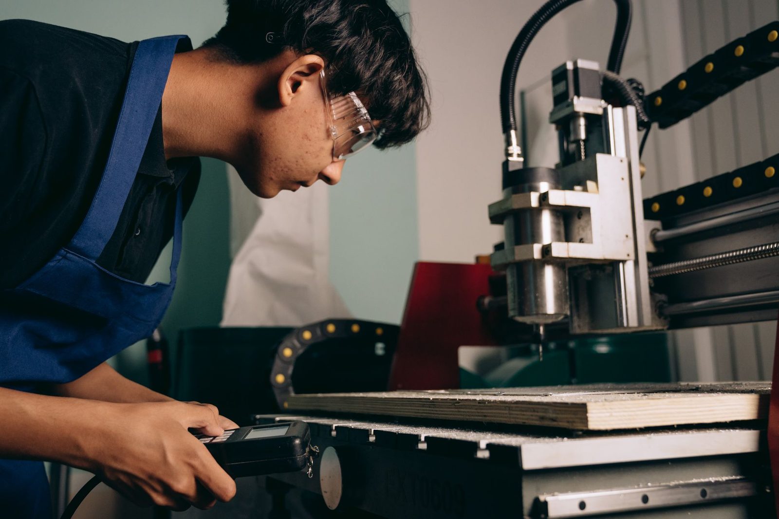 Jeune apprenti en salopette bleue et lunettes de protection réglant une machine-outil à commande numérique en atelier
