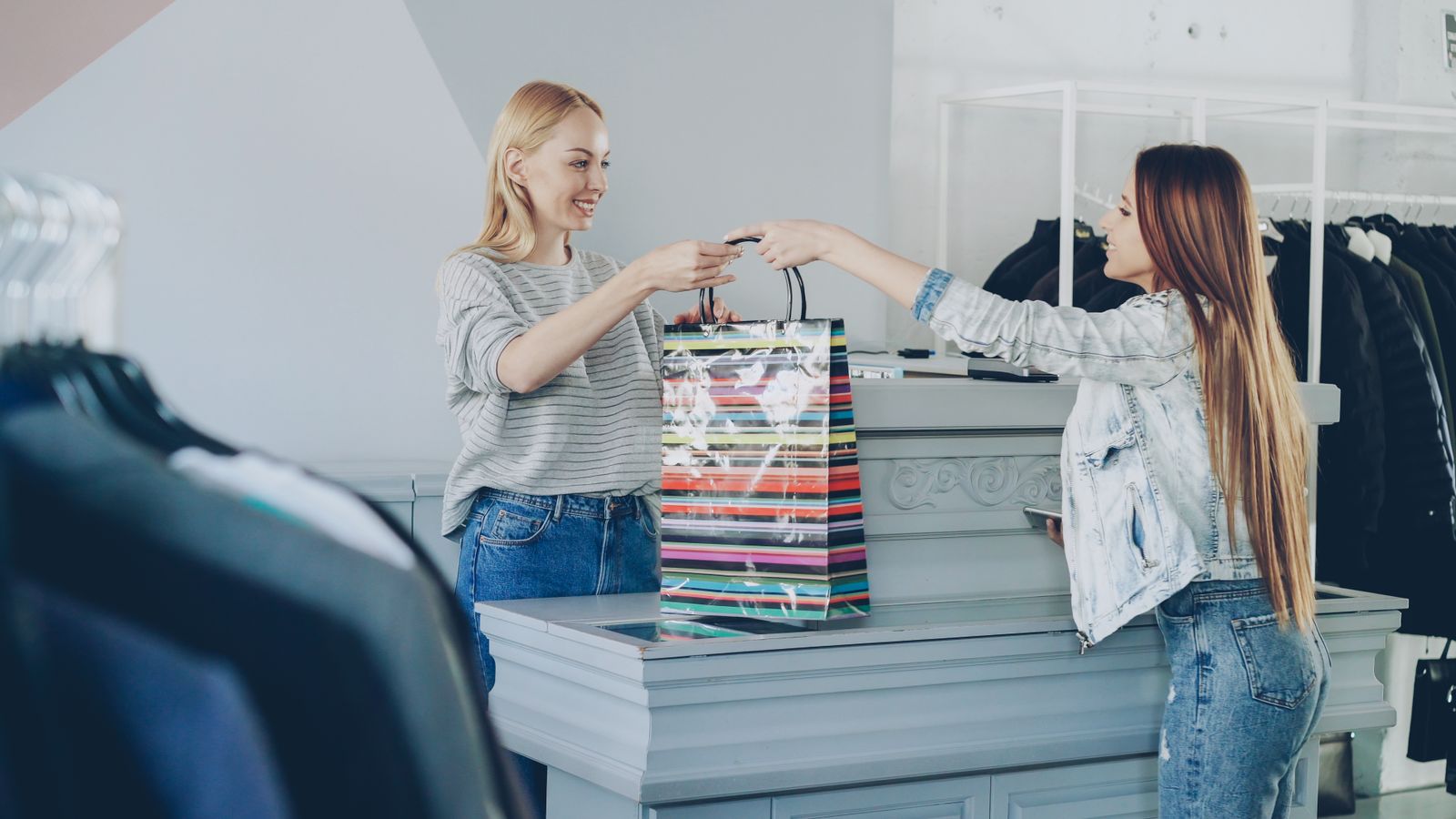 Commessa che consegna un acquisto a una cliente al bancone di un negozio di abbigliamento, a illustrazione dell'alternanza nel commercio e nelle vendite