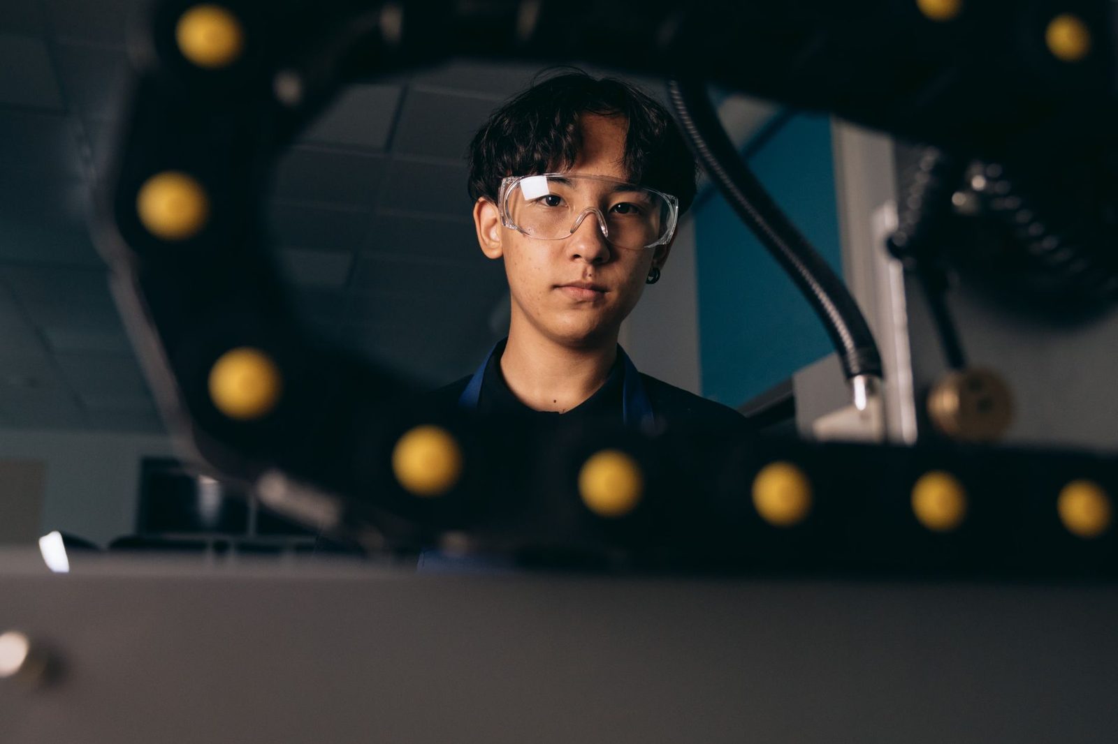 Jeune homme avec lunettes de protection derrière un bras robotisé dans un atelier technique