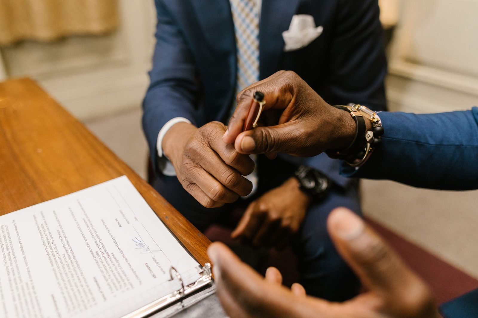 Two men in suits handing over a pen above a contract lying in a folder on a table