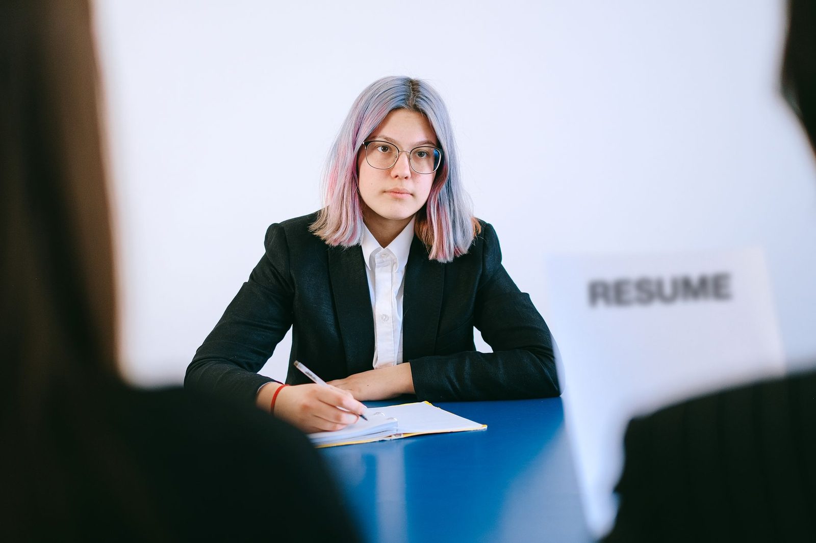 Een vrouw met gekleurd haar en een bril tijdens een sollicitatiegesprek, met een cv op tafel.