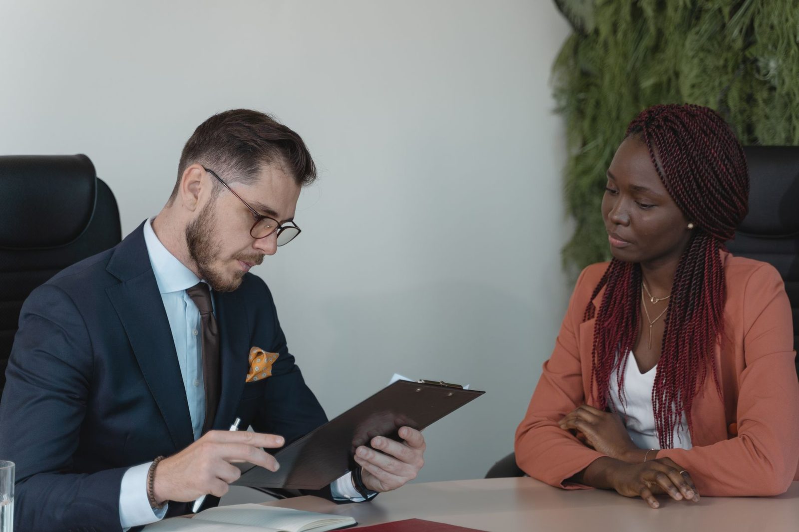 Recruteur en costume lisant un CV sur un porte-bloc face à une jeune candidate lors d'un entretien