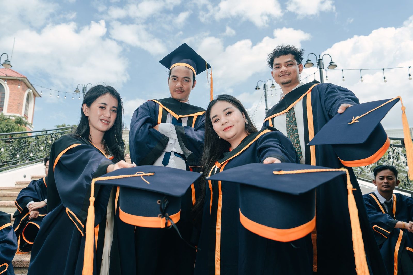 Jeunes diplômés en toge tendant leurs toques noires et orange vers l'objectif en extérieur