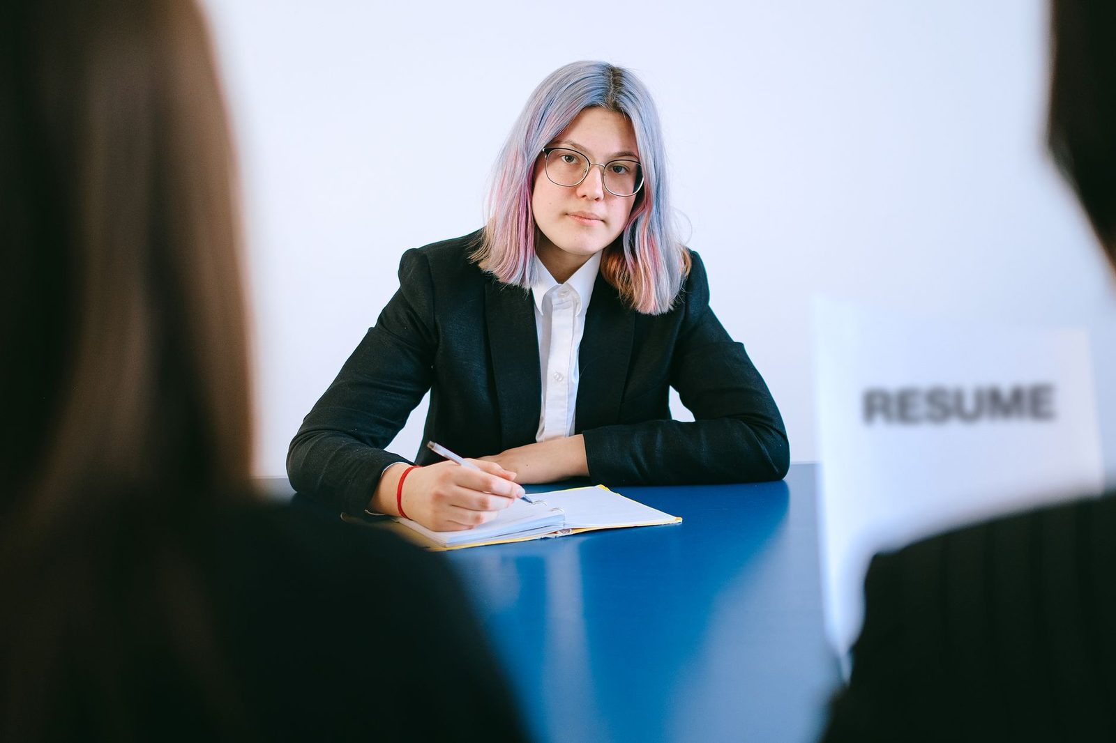 Jeune candidate en veste noire face à deux recruteurs lors d'un entretien d'embauche, CV posé sur la table