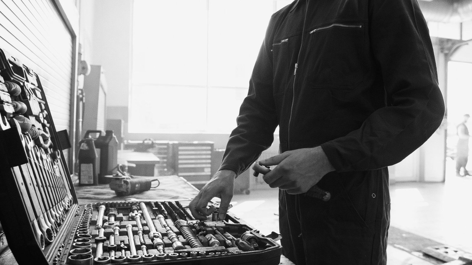 Technicien en combinaison choisissant un outil dans une caisse à douilles dans un atelier, photo noir et blanc
