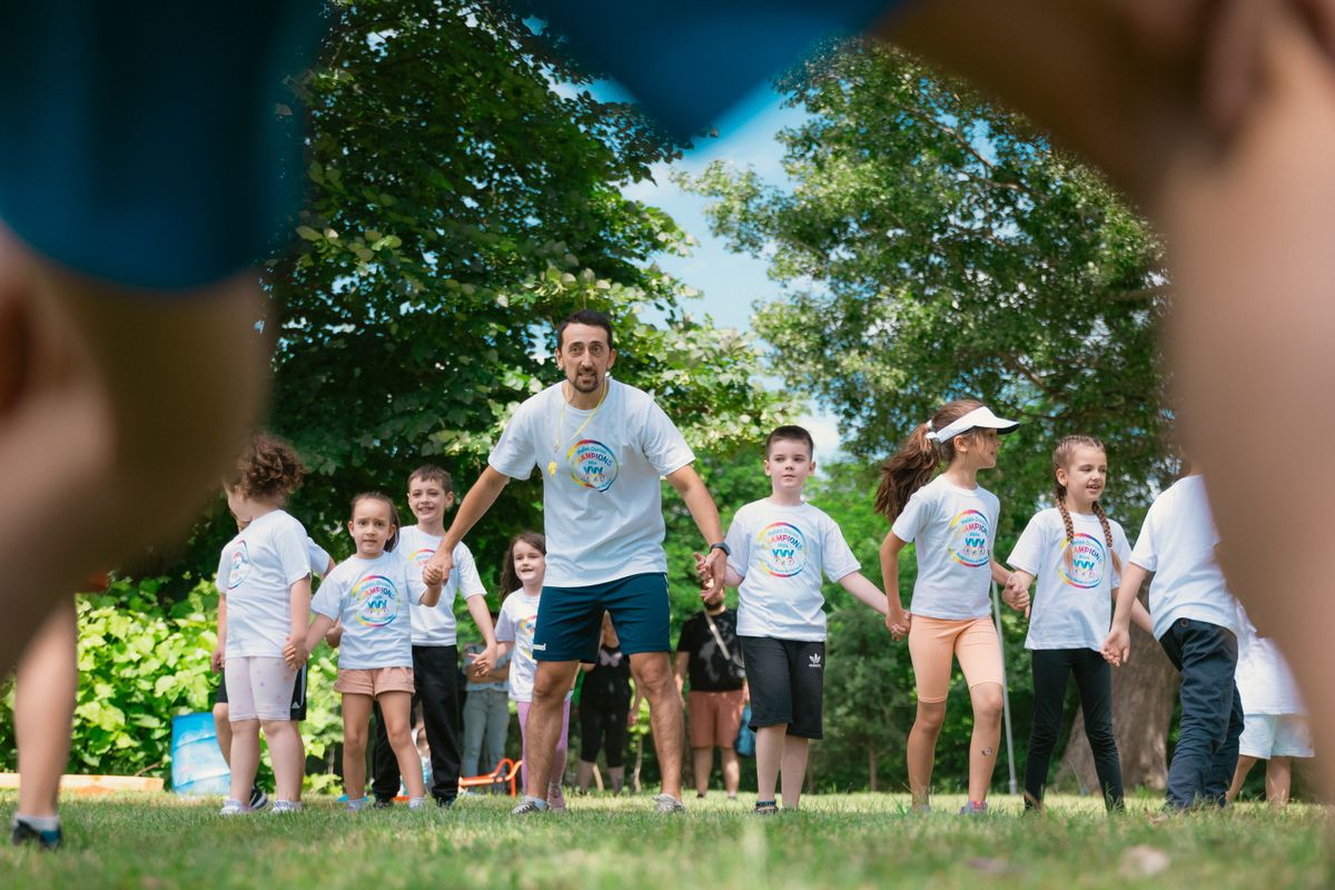 Gruppo di bambini che pratica un'attività sportiva guidata da un educatore in un parco soleggiato, che illustra l'animazione sportiva d'estate