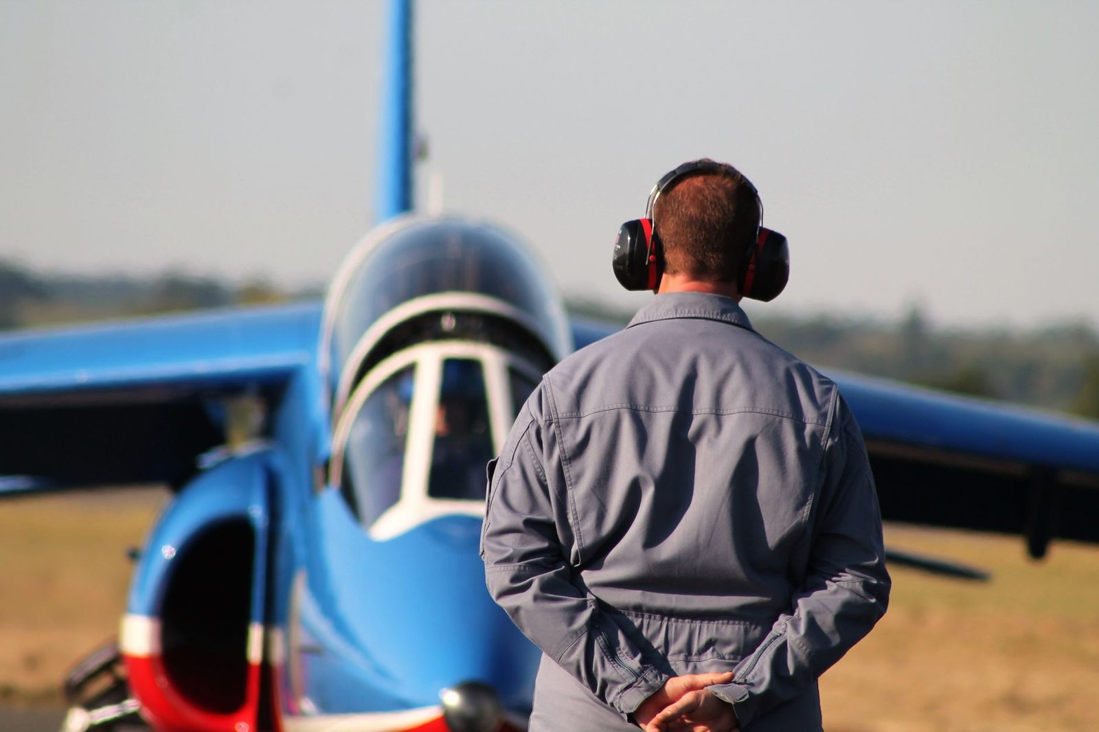 Technicus in grijze overall met gehoorbescherming voor een blauw vliegtuig op het platform