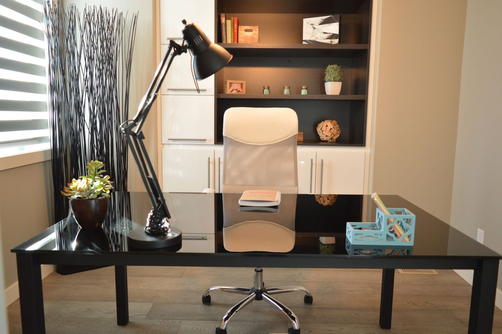 Bureau noir vide avec lampe articulée, chaise ergonomique blanche et étagères dans un espace de travail