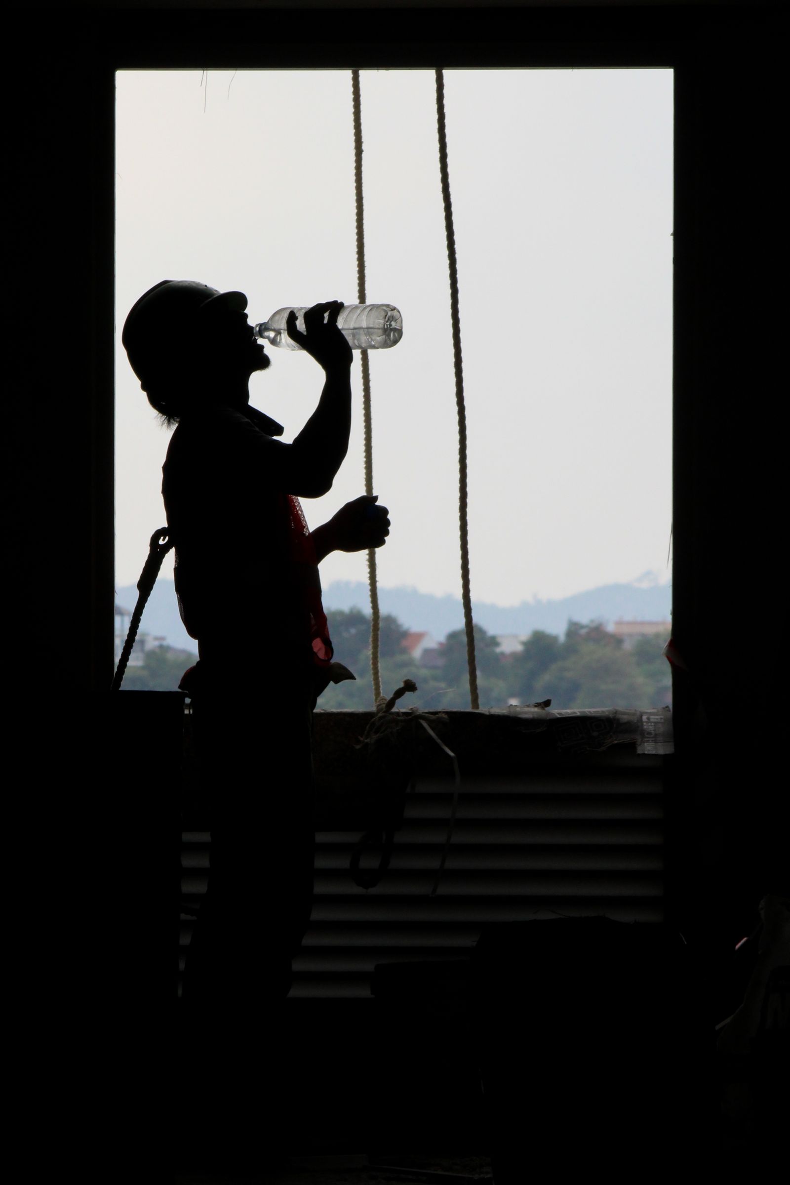 Silhouette of a construction worker hydrating on a worksite in full sun, illustrating summer working conditions for outdoor apprentices