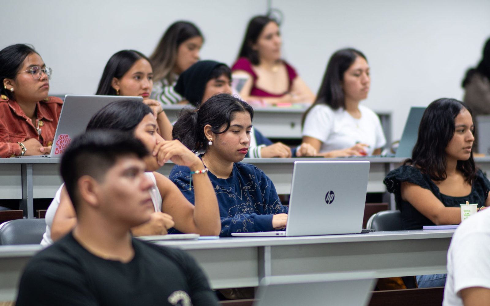 Estudantes sentados numa sala de aula com computadores portáteis abertos nas suas secretárias.