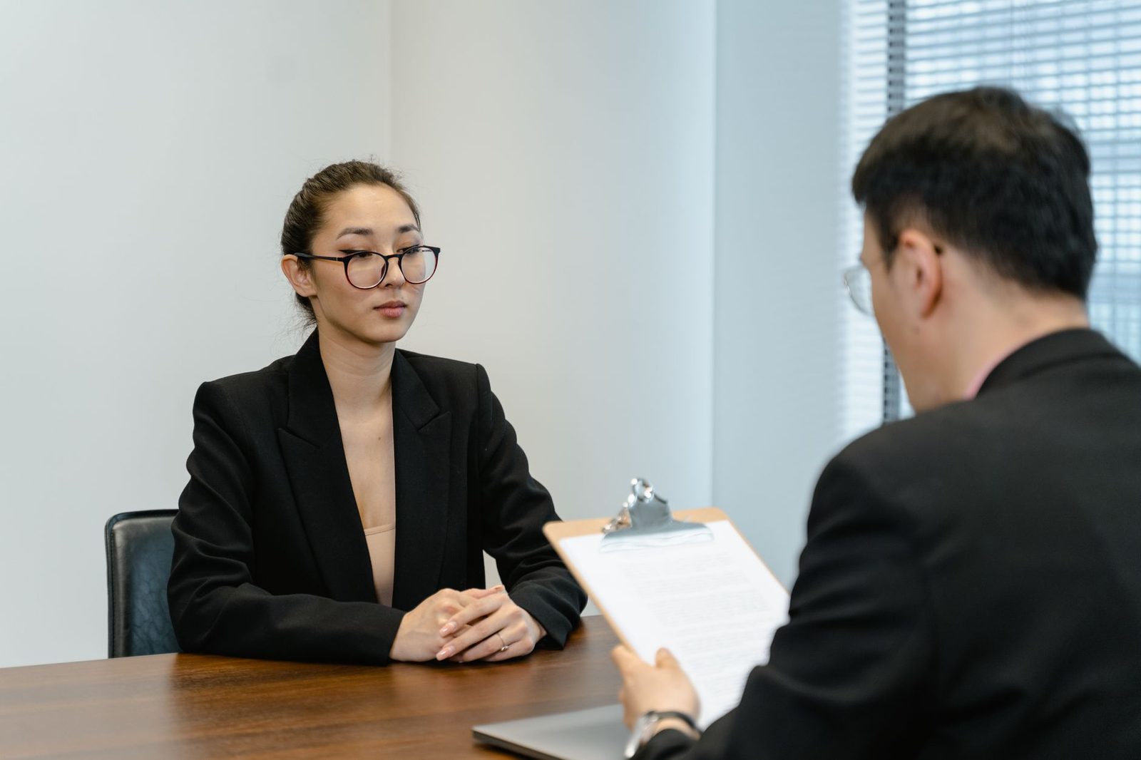 Uma jovem mulher com óculos e blazer preto durante uma entrevista com um homem de fato.