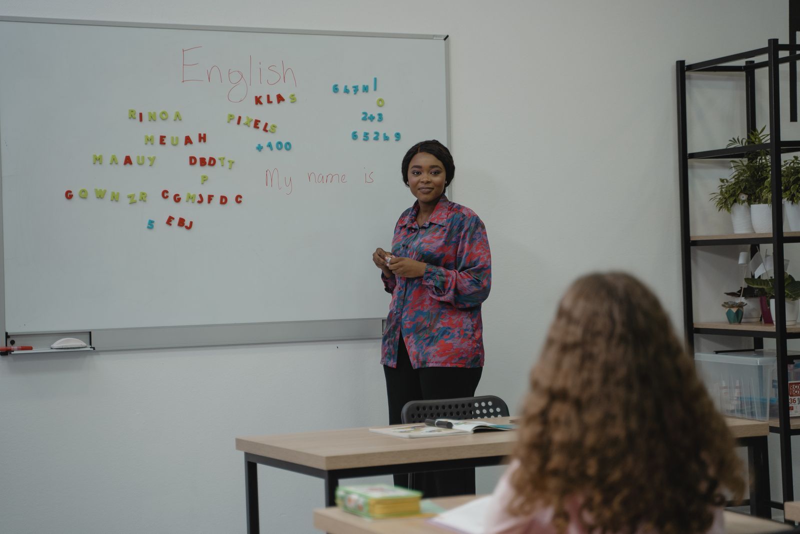Teacher explaining a lesson to a student in front of a whiteboard in a bright classroom