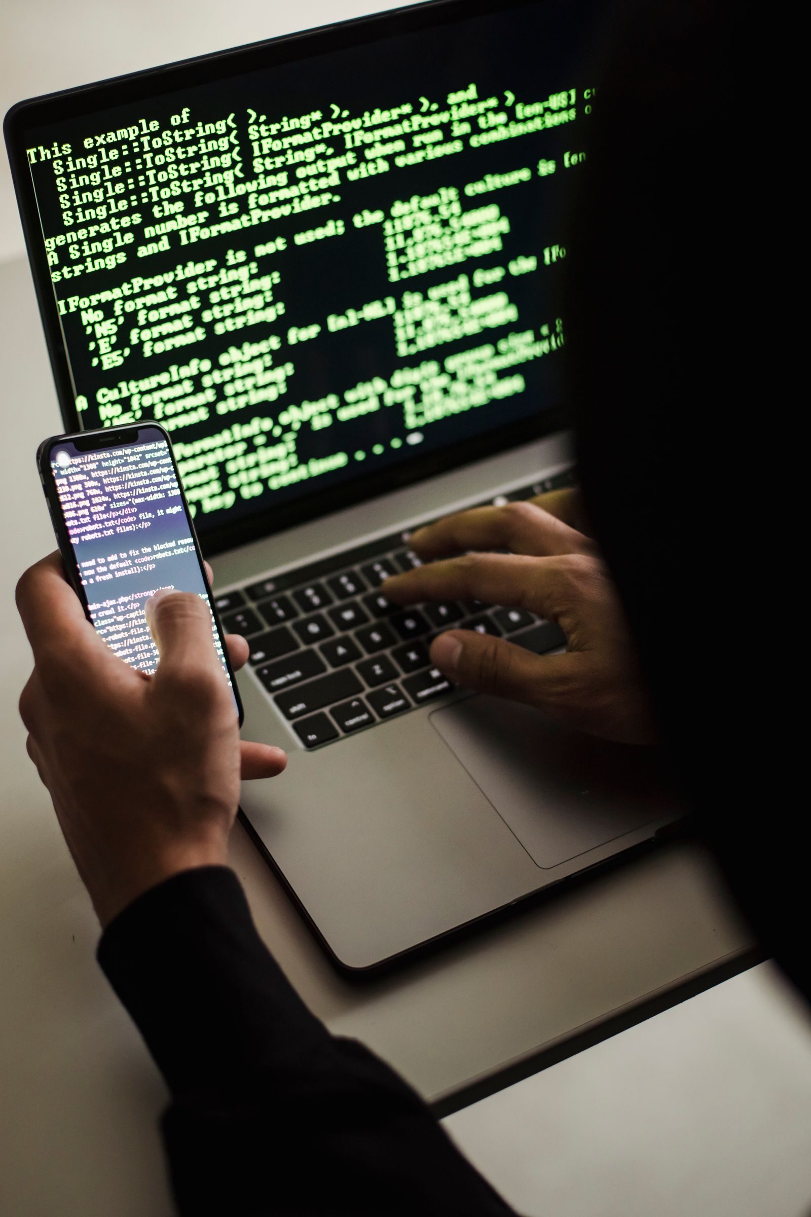Silhouette de hacker masqué tapant sur un ordinateur portable dans un environnement sombre, illustrant la menace cyber