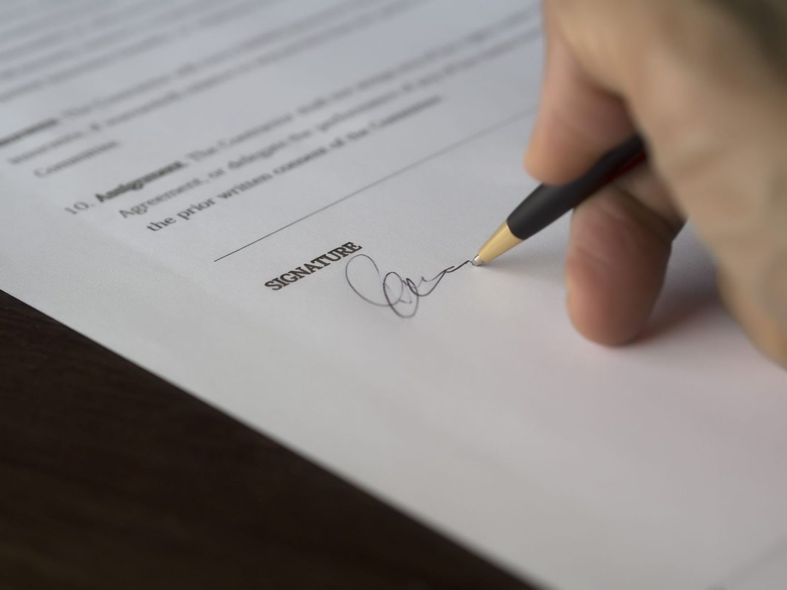 Main signant au stylo la ligne « signature » d'un contrat papier posé sur une table en bois