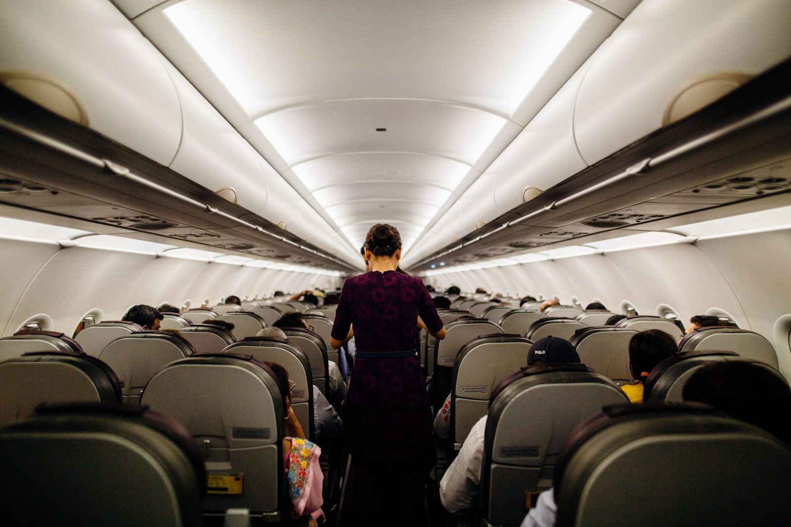 Assistente de bordo de pé no corredor de uma cabina de avião cheia de passageiros sentados
