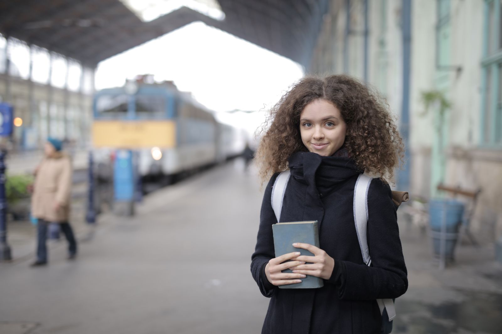 Giovane donna con uno zaino e un libro in attesa su una banchina, a illustrare la partenza per una mobilità internazionale durante un'alternanza