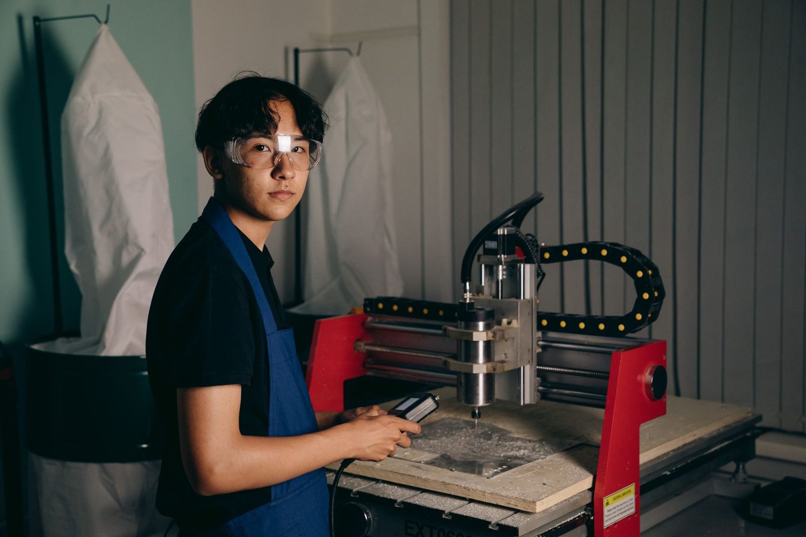 Jeune apprenti en tablier bleu et lunettes de protection utilisant une fraiseuse à commande numérique en atelier
