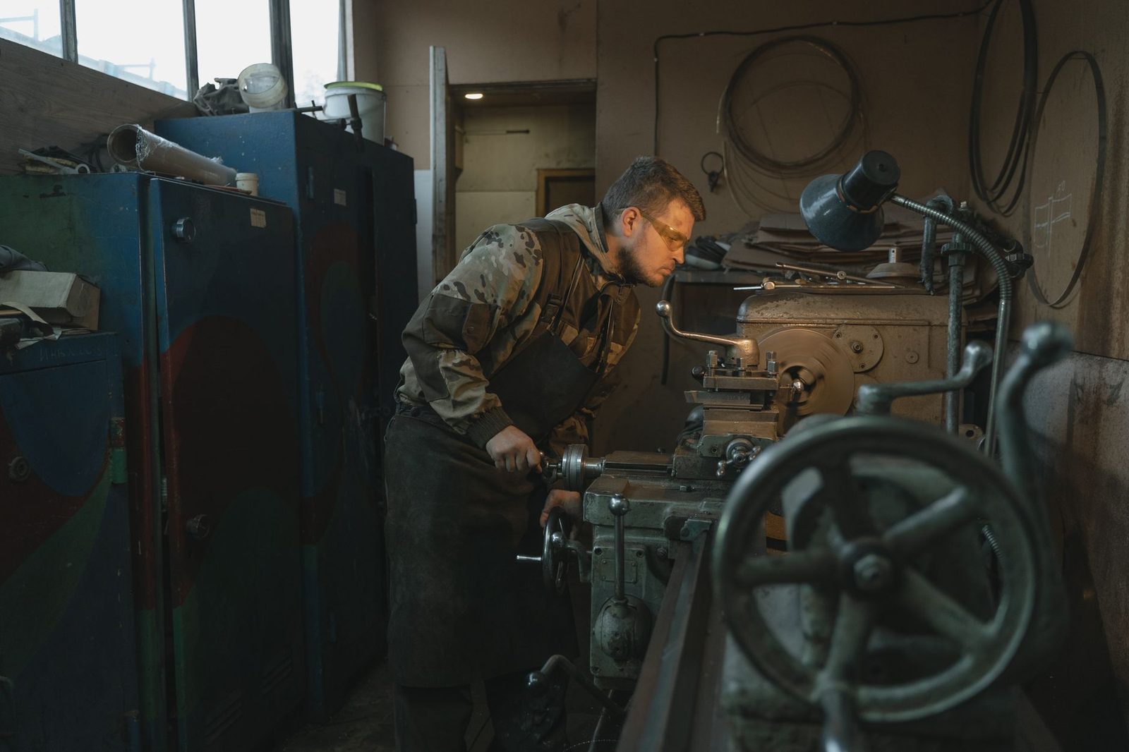 Jeune homme avec lunettes de protection et tablier travaillant sur un tour dans un atelier d'usinage
