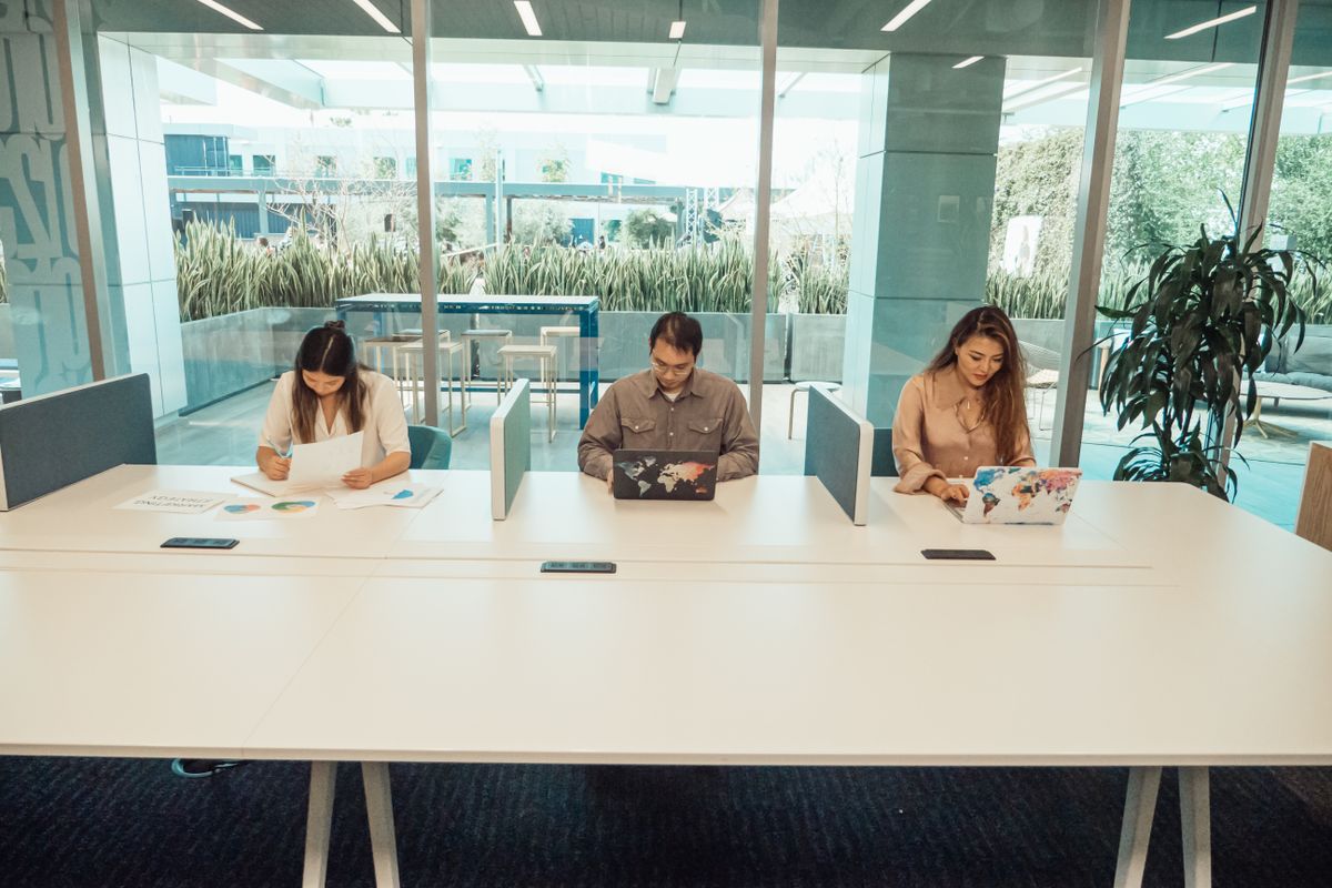 Three colleagues collaborating at a meeting table, illustrating work-study in an open space in a large company