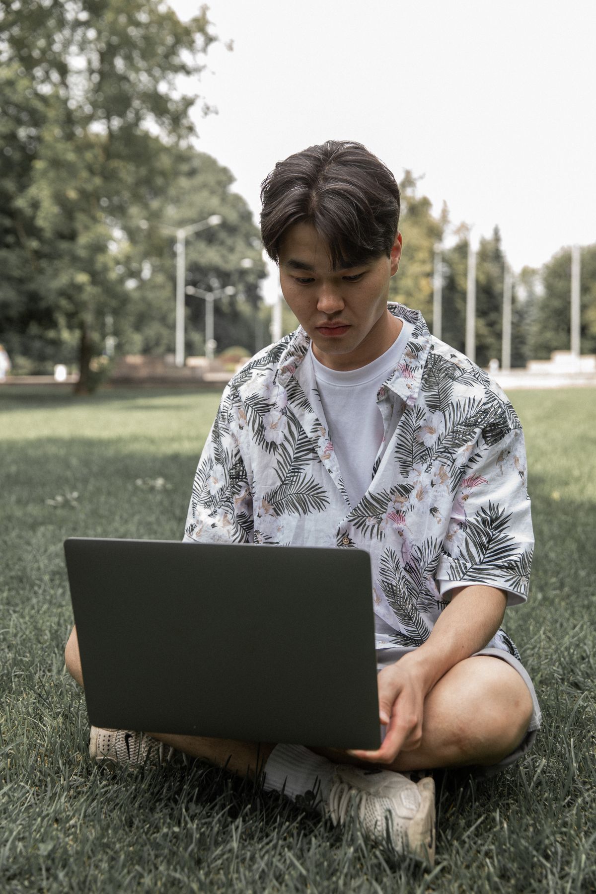 Aprendiz concentrado no seu computador portátil, sentado na relva para avançar na sua procura durante o verão