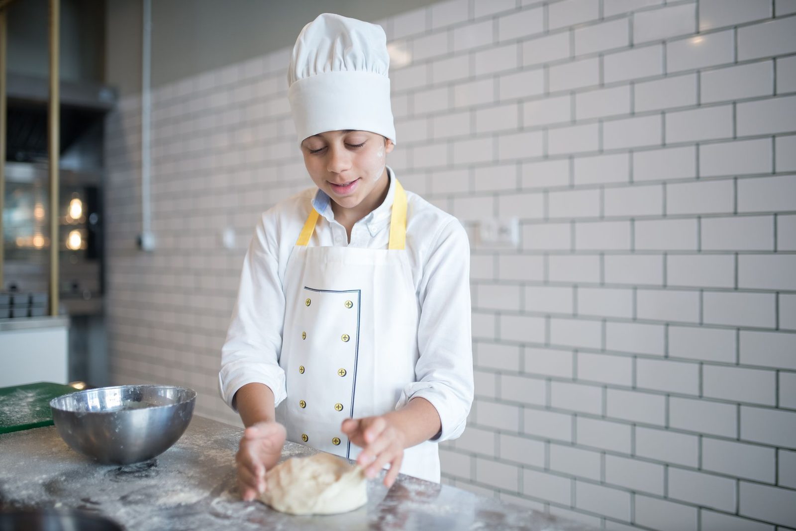 Jeune apprenti en toque et tablier blancs pétrissant une pâte sur un plan de travail fariné