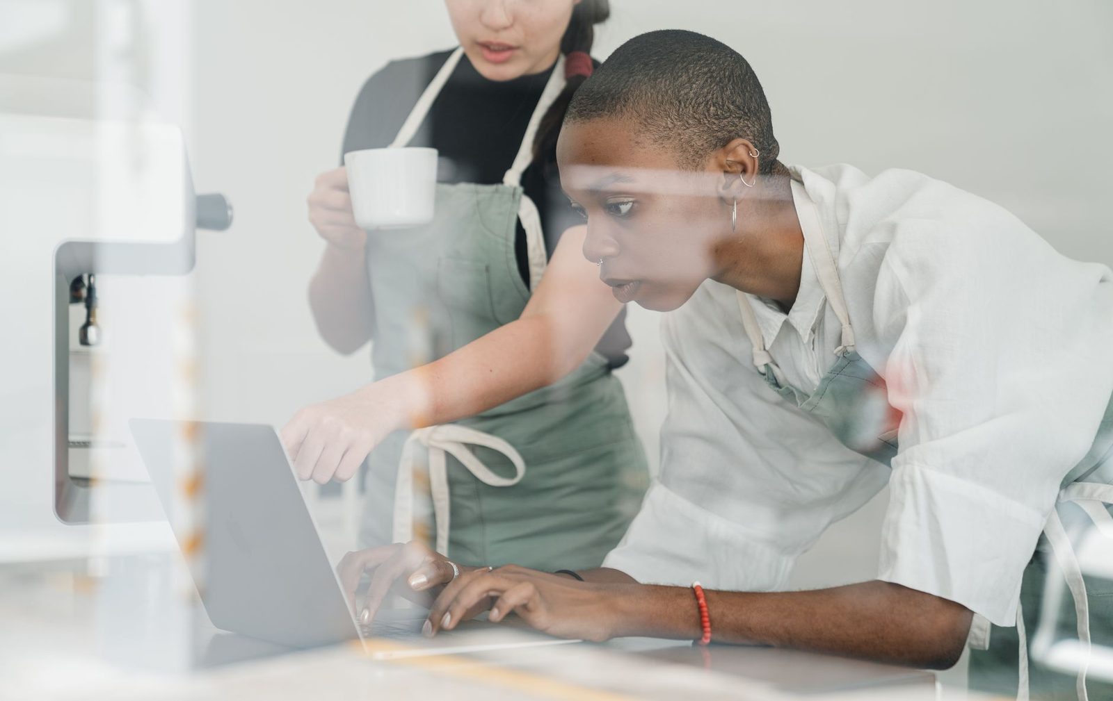 Jeune employée en tablier travaillant sur un ordinateur portable, accompagnée d'une collègue tenant une tasse